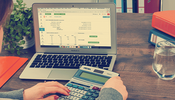 Rapariga em frente a computador portátil com calculadora nas mãos